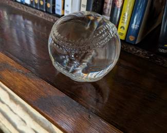 A unique and decorative piece for any baseball fan or desk! This is a solid, clear glass paperweight shaped and etched like a baseball. It's a great accent for a home office, a man cave, or a gift for a sports lover.