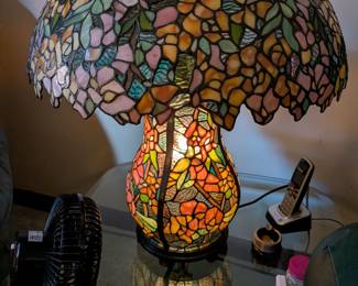 This is a magnificent and artistic table lamp in the iconic Tiffany style. The lampshade and the base are both crafted from beautiful, multi-colored stained glass in a stunning floral motif. The lamp features a unique dual-light function, allowing the top, the base, or both to be lit at once, creating a truly spectacular glow. This is a one-of-a-kind statement piece that will be the focal point of any room.