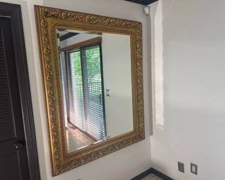 Oversized wall mirror in a baroque-style gold leaf frame with carved floral details.