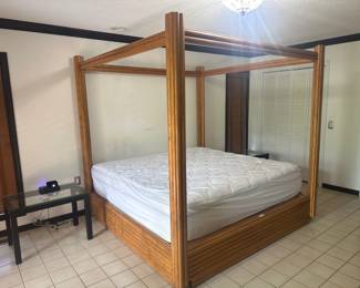 Modern four-poster king canopy bed frame in warm wood tone with clean, sleek lines.