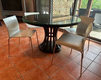 Sleek round glass dining table with sculptural wood base and four minimalist white chairs