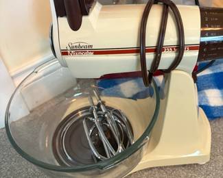 Classic Sunbeam Mixmaster 235-watt stand mixer with original glass mixing bowl and chrome beaters. Retro two-tone cream and brown finish.