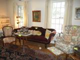 Living room: Large antique sofa (original to house), chintz print wing chair, striped ladies parlor chair, Eastlake style marble topped table with silver (plate) tea service. One of two room sized oriental rugs visible on floor.