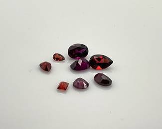 Assorted garnet gemstones of mixed shapes and sizes. The large teardrop stone has a chip.