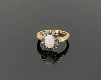 Oval opal cabochon surrounded by (8) round cut dark blue tourmaline arranged in a flower pattern. Stamped "SCBS 10K". Size 8. 2.86 gtw.