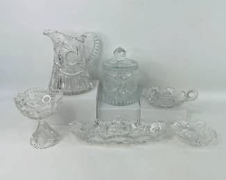 Lot includes an assortment of vintage cut glass pieces, comprising of one biscuit jar (H 8" x W 5 1/4"), one 8" pitcher, one handled candle plate, one celery dish, and additional similar items. Pitcher has chip on spout. Small dish/ashtray is chipped. See photos for details. Shipping-NO