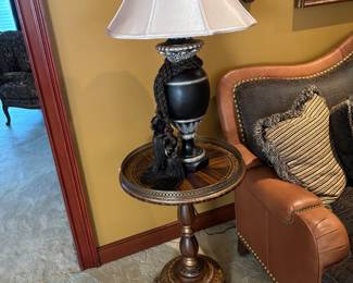 Accent Table – Ornate round accent table with rich wood tones, inlaid design, and carved pedestal base with claw feet. Elegant and versatile, perfect for a living room or study.
Decorative Lamp – Black and gold lamp with sculptural detailing, fabric shade, and elegant trim. A refined lighting piece that adds warmth and style to any space.