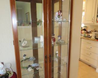 Narrow curio cabinet, glass shelves, mirrored back and lights.