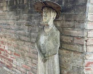 Side view of Hand-carved wood sculpture of a gardener with a quote from American author and environmentalist Wendell Berry 'I farm the soil that yields my food. I share the creation. Kings can do no more.' from Wendell Berry's poem "The Farmer, to His Wife" from his "Collected Poems, 1957–1982" published in 1985.