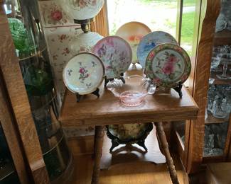 Various collection of flower plates and gone with the wind style lamp on a tiger Oak parlor table