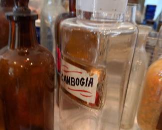 Vintage amber apothecary bottle alongside clear glass jar labeled "Mossga" with glass stopper; classic pharmacy bottles for display or collection.