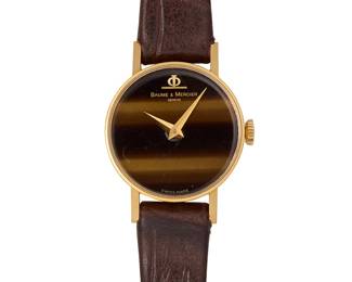 284
Baume & Mercier: A Gold and Tiger's Eye Watch
Dial: 20.00 mm, round tiger's eye with no hour markers
Case: 21.40 mm
Case number: 656516, 36636 2
Closure: a brown leather strap with gold buckle clasp
Signed: dial and clasp

Inner circumference: 6 - 7 1/2 in.
16.4 grams gross
Estimate: $600 - $800