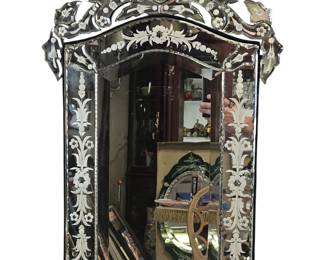 This exquisite wall mirror is a magnificent example of Venetian-style glass artistry, a tradition celebrated for its unparalleled elegance and meticulous craftsmanship. Composed of multiple panes of beveled and etched glass, the mirror's ornate frame and distinctive crest top give it a sculptural, almost architectural quality. The intricate floral and scrollwork designs etched into the glass catch the light, transforming the mirror from a simple reflective surface into a captivating work of art. This piece would serve as a stunning focal point in any room, bringing a touch of timeless sophistication and old-world glamour.
