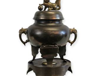 This is a magnificent and rare antique piece, a large and highly detailed bronze vessel that is a beautiful testament to East Asian craftsmanship. The piece is comprised of a multi-part design, including a substantial bowl with stylized mythological animal handles, a fitted lid, and a decorative stand and base. The most striking feature is the lid's finial, which is a charming and intricately sculpted figure of a dog-like creature, possibly a "foo dog," playing with a ball. This vessel is a commanding sculptural work of art and a truly rare find for collectors of fine Asian antiques and ceremonial objects.
