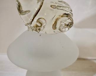 A clear glass frog figurine sitting on top of a frosted glass mushroom