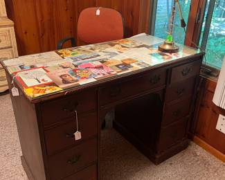 Vintage Wooden Office Desk – Classic double-pedestal desk with nine drawers, brass pulls, and a glass top protector. The glass surface is decorated with vintage magazine and postcard clippings, giving it a one-of-a-kind look. Solid construction, perfect for a home office, craft space, or study.
Mid-Century Style Desk Lamp – Brass adjustable desk lamp with swivel shade, ideal for task lighting or adding a retro touch to your workspace.
Office Chair – Padded swivel office chair with orange upholstery, functional and comfortable for everyday use.
✨ Solid, heavy vintage desk with character.
✨ Great for home office, studio, or study space.
✨ Unique glass top design – must-see piece!