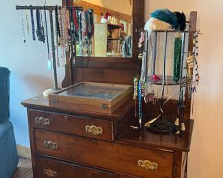 Antique Dresser with Mirror – Beautiful wooden dresser featuring ornate carved details, a tall beveled mirror with decorative crest, and multiple drawers with brass pulls. Solid craftsmanship with both storage and display appeal.
Vintage & Costume Jewelry Collection – Large assortment of necklaces, beads, and accessories displayed on racks. Includes colorful costume pieces, vintage beaded strands, and statement jewelry.
Jewelry Display Cases & Racks – Wooden glass-top jewelry case and freestanding jewelry racks filled with assorted pieces.
✨ Gorgeous antique dresser with original mirror.
✨ Great opportunity for jewelry collectors and resellers.
✨ Unique combination of fine furniture & jewelry display!
