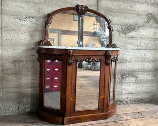 This lot features a Victorian Rococo Revival credenza, circa 1850 with mirrored cabinet doors, a marble top and mirror. Measures with mirror, 56.5” H x 46.5” W x 16” D.
