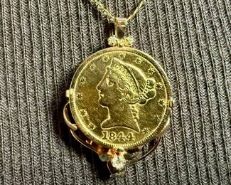 This lot features a 1844 $5 Liberty Head gold coin in a 14k gold setting with two small diamonds above and one larger diamond below. Sits in a 14k gold chain, both items marked as shown in photos. Total approx. weight is 13.15 grams with a 18” chain. 340,330 mintage.
