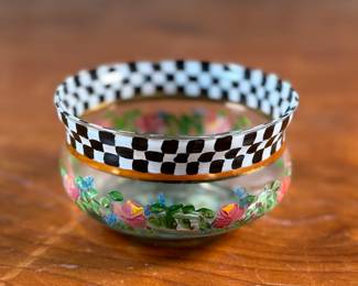 This lot features a vintage hand painted bowl by Victoria & Richard Mackenzie-Childs. Maker mark underneath as shown in photos. The MacKenzie-Childs story began with Victoria and Richard MacKenzie-Childs in 1983, creating hand-painted ceramics in rural New York, a style later called “tradition with a twist” and inspired by the couple’s daughter. After facing bankruptcy in 2000 due to financial issues, the brand was acquired in 2001 by Pleasant Rowland, founder of the American Girl doll company. Despite a subsequent dispute and the founders’ departure, MacKenzie-Childs is now a thriving luxury home decor company known for its signature Courtly Check pattern and other whimsical, handcrafted designs.  
