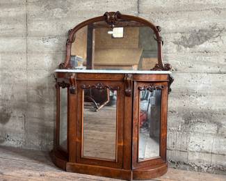 This lot features a Victorian Rococo Revival credenza, circa 1850 with mirrored cabinet doors, a marble top and mirror. Measures with mirror, 56.5” H x 46.5” W x 16” D.
