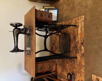 This is an antique Singer treadle sewing machine with ornate gold detailing and original oak cabinet with side drawers. The cast iron treadle base is intact, making it both a functional piece for sewing enthusiasts and a sought-after decorative collectible.