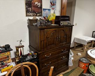 This is a vintage wooden highboy dresser with ornate brass hardware, carved panel doors, and multiple drawers for storage. Solidly built and detailed, it’s both a functional storage piece and a statement furniture item.