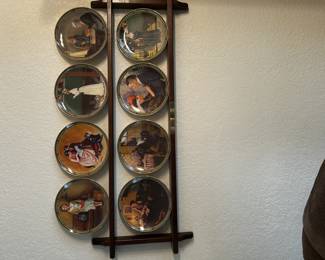 This is a set of collectible Norman Rockwell plates displayed on a two-tier wooden wall rack. Each plate features a classic Rockwell illustration, making the collection perfect for Americana fans and collectors of decorative plates.