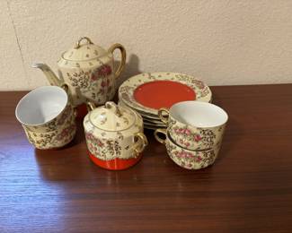 This is a vintage floral porcelain tea set with gold trim, featuring a teapot, sugar bowl, several cups, and matching plates with striking red centers. Likely mid-20th century, these sets are both collectible and functional, adding elegance to display or tea service.