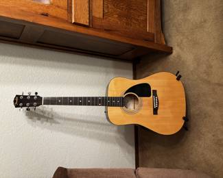 This is a Fender acoustic guitar with a natural finish and black pickguard, classic dreadnought body style. Fender acoustics are reliable instruments, great for both beginners and casual players, while also collectible as a well-known brand.