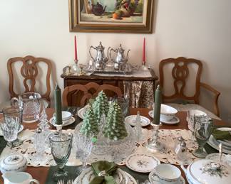 The center of the dining room table with 6 newly upholstered chairs.  Above the small cabinet is a beautiful framed art signed with a sterling silver plated tea/coffee set.  The table is set with a 8 piece place setting of gorgeous China by Flaire.