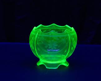 Seen under blacklight: An EAPG uranium vaseline glass rose bowl with wheel cut floral design, on tabbed feet