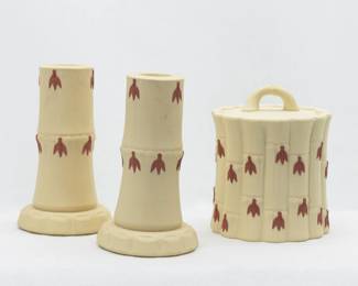 A Wedgwood Primrose yellow Jasperware covered sugar jar and pair of candlesticks from the bamboo or cane ware pattern. Crafted with a vertical bamboo stalk design as the body of the pieces, with small applied terracotta colored leaves emanating from each of the indentions representing joints. The lidded sugar jar 4.5” H x 3.5” W, candlesticks 4.5” H x 2.5” widest part.