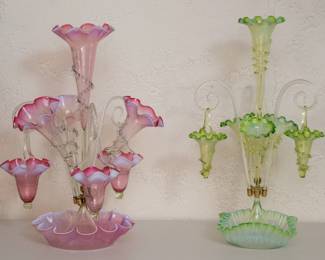 Antique Victorian era art glass epergnes or centerpiece vases, the first a 4-trumpet epergne with 3 hanging baskets, cranberry uranium vaseline glass; trumpet horns with ruffled top rim and hand applied clear rigaree on the neck, the baskets with ruffled rims and hand applied handles above a round base with crimped edges. The second antique 19th century art glass epergne has three vaseline uranium glass trumpets around a taller central trumpet, and three spiral canes suspending three baskets, all with crimped ruffled edges above a squared base with crimped edges.