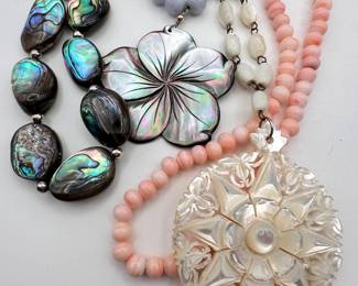 Closeup of beautiful necklaces with carved mother of pearl and abalone shell pendants and beads, and polished natural stone beads