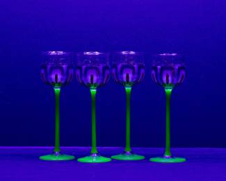 Seen under blacklight: A set of four antique Art Nouveau hand blown wine goblets with Uranium Glass stems and hand painted crystal bowls, c 1900, probably Hohes Stängelglas Meyr's Neffe.