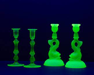 Seen under black light: A pair of Cambridge Emerald Dolphin frosted uranium glass candlestick holders, and a pair of EAPG green uranium glass candlestick holders