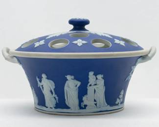 Another view of the Wedgwood blue jasperware lidded potpourri pot featuring applied white sprigs creating a bas-relief frieze of classical figures around the outside, and two white handles. The lid also features white bas-relief decoration and a raised finial on the top. A post-1930s mark to base of “WEDGWOOD” and “Made in England” and potter’s mark. 4.5” tall to height of knob, 7” across handle to handle, 6” across the rim. 