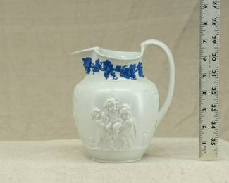 Antique Wedgwood "Bacchanalian Boys" pitcher, white jasper, decorated with Classical imagery of young boys and satyrs in Bacchic revelry (with grapes and grape leaves in their hair.) On one side, a young Bacchus holding his thyrsus (fennel staff) is being held aloft by two other boys, a vessel of wine beside them; the other scene has a satyr and young Bacchus sitting beneath a tree. The neck of the pitcher has applied blue sprig band of fruiting grape vines. Marked with "WEDGWOOD" to the base, dating 1790 to 1820. The design is based on drawings sent to Josiah Wedgwood by artist Lady Diana Beauclerk, née Spencer (1734-1808), daughter of the 3rd Duke of Marlborough.