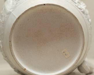 Closeup of the base of the early 19th century Wedgwood smear glazed white pitcher decorated with finely modeled jasper applied to depict a hunting scene, and with dark blue jasper grapevines applied around the top rim