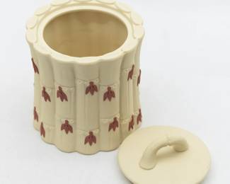 Closer look at the A Wedgwood Primrose yellow Jasperware covered sugar jar and pair of candlesticks from the bamboo or cane ware pattern. Crafted with a vertical bamboo stalk design as the body of the pieces, with small applied terracotta colored leaves emanating from each of the indentions representing joints. The lidded sugar jar 4.5” H x 3.5” W, candlesticks 4.5” H x 2.5” widest part.