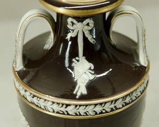 Closeup of the antique 1850's Wedgwood black dip jasper ware double handled urn shaped vase with applied classical figures in white relief depicting the muses of comedy/drama, music, poetry; covered overall in a shiny clear glaze and with applied gilding. Wedgwood stamp to the base along with group of 4 "mustache" marks, and hand-incised numerals 350. See example in of this vase in the Nelson Provincial Museum, Australia.
