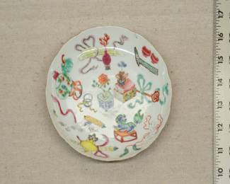 A Chinese export porcelain famille rose enameled dish decorated with various items including books, a ruyi staff, scroll, incense censer, fish bowl, peony, and a wrapped guqin (a seven-string zither.) The reverse decorated with flying bats in iron red, with six-character mark to the base.