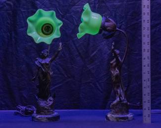 Seen under blacklight: A graceful pair of antique French Art Nouveau era bronzed spelter figural lamps on marble bases, the sculpted female figure of Victory in flowing robes, with the lamp a rising stem supporting a hand-blown uranium glass flower form shade.  The word "Victoire" is on the front base of the figures, and both have the signature of artist Rucho Pse along with a stamp mark reading Paris Made in France.