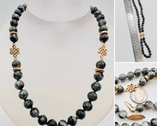 A necklace of polished natural black and gray stone beads with two gold tone Chinese knot spacers and a 14k yellow gold clasp