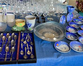 Collectible spoons, small glass bowls, glass candy dishes, sparkling gold and blue swirled glass bowl, ceramic figurines, ceramic frog with small yellow bowl on top, white tray with a black trim, decorative blue plates with animals on them (lion, penguin, horses, etc)