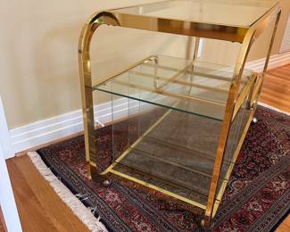 L3 - $750. Milo Baughman Brass and Glass 3 Tier Bar Cart. Measures 46.5" x 18" x 28" tall. The bottom right piece of glass has a chip we didn't notice until we were looking at it for issues. The glass could be replaced but if there is something near it you can't see it. 