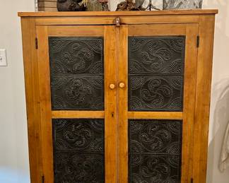 Primitive Punched Tin Pie Safe / Cabinet
Charming primitive pie safe featuring warm wood construction with classic black punched tin panels on both doors. The tin features a swirling fern motif, adding rustic character and traditional farmhouse appeal.

Inside are three shelves, perfect for storage or display of kitchenware, collectibles, or décor. This piece blends functionality with authentic country style and would look equally at home in a farmhouse kitchen, cabin, or rustic lodge.

Condition: Good vintage condition with age-appropriate wear that adds to its charm. Solid and sturdy.

Dimensions: Approx. 40” W x 54” H x 16” D