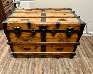 Antique Steamer Trunk with Iron Hardware
Beautifully aged steamer trunk featuring solid wood construction with black wrought-iron hardware, latches, and corner braces. The trunk opens to a spacious interior with an old-world look, perfect for storage or as a decorative statement piece at the foot of a bed, in a living room, or as a unique coffee table alternative.

Its warm finish and sturdy iron accents give it a timeless rustic appeal that blends seamlessly with lodge, farmhouse, or vintage décor.

Condition: Good antique condition with age-appropriate wear and patina that enhance its character. Functional latches, sturdy build.

Dimensions: Approx. 34” L x 21” W x 22” H