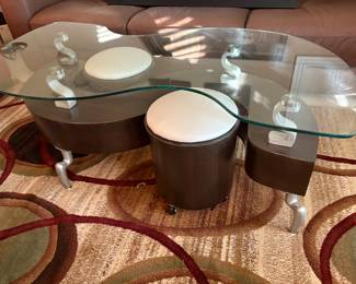 Contempory S Shape Glass top Coffee table with two stools on casters.  Notice legs and glass supports.  Beautiful rug.
